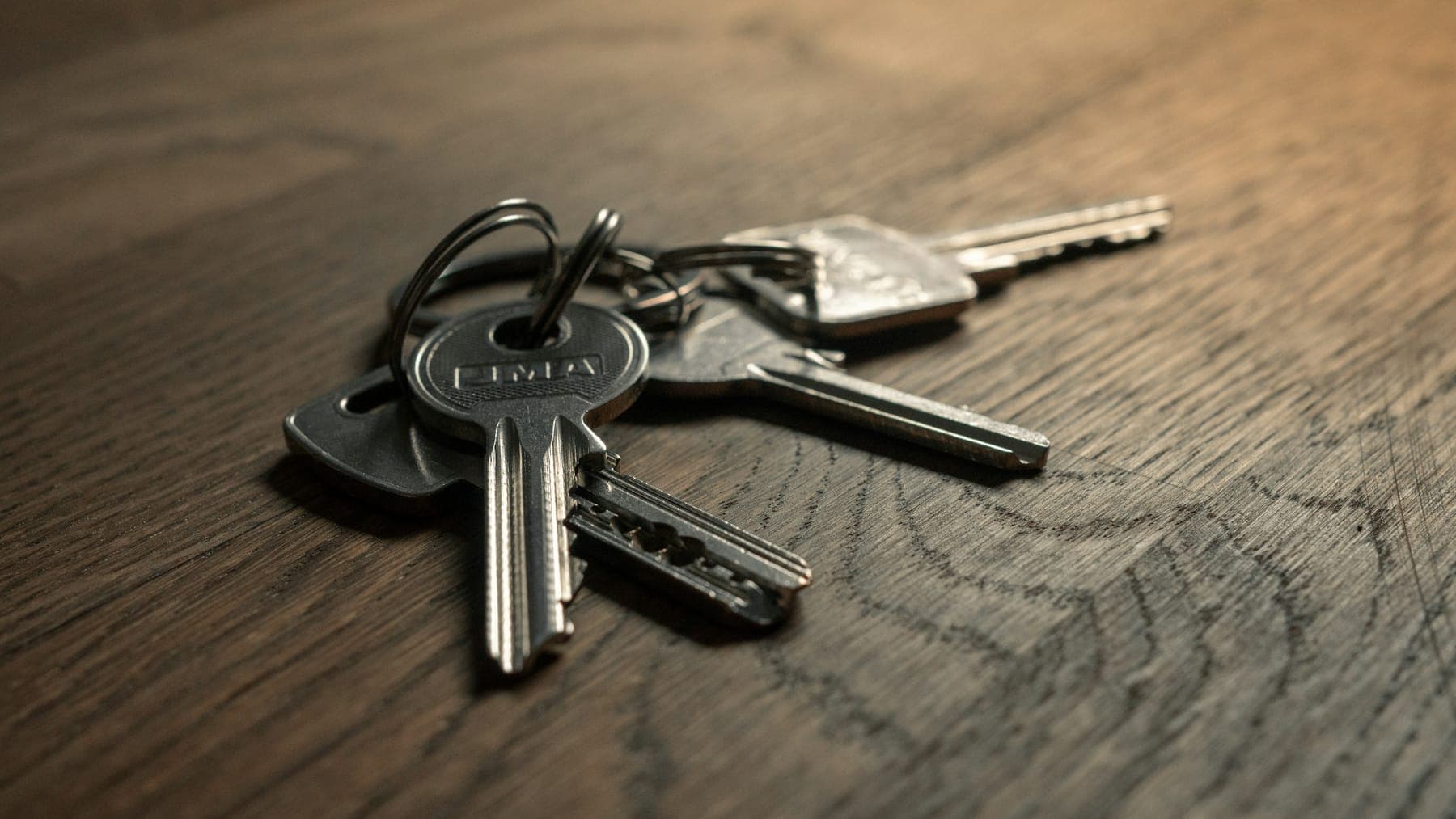 A bunch of keys on a dark wooden table in warm, low light.